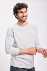 Remera de manga larga color gris claro jaspeado, con cuello redondo de terminación a la base (sin ribete). Presenta costuras tipo raglán en los hombros.