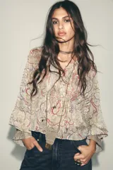 Camisa estampada con motivos paisley en tonos beige, rosa, lila y amarillo. Tiene cuello redondo con lazos, mangas largas abullonadas con puños elásticos y volantes en el delantero.