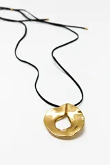 Collar con cordón negro y dije dorado con forma orgánica.