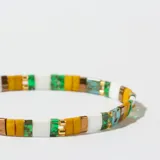 Pulsera elástica con cuentas rectangulares de colores amarillo, blanco, verde y celeste, separadas por pequeñas cuentas doradas.