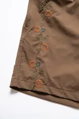 Short de baño marrón con bordado de enredadera en la pierna izquierda, cintura elástica con cordón ajustable, bolsillos laterales y bolsillo trasero con cierre.