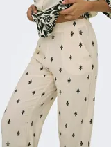 Pantalón de pierna ancha color crema con estampado de hojas negras, cintura elástica trasera y bolsillos frontales.