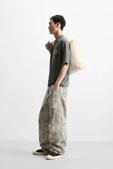 Camiseta gris oscuro con efecto lavado, cuello redondo y manga corta. Tiene un bolsillo en el pecho y estampados en el frente y la espalda.