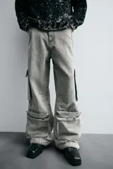 Pantalón relaxed fit de denim negro con efecto lavado, bolsillos frontales, traseros de plastrón y multifunción en perneras. Bajo ajustable con trabilla y cierre frontal con cremallera y botón.