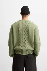 Sweater verde claro de punto con cuello redondo y mangas largas. Presenta diseño de trenzas en el centro y en las mangas.