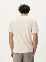 Camiseta blanca de algodón con cuello redondo y mangas cortas. Estampa rectangular con borde negro que contiene la frase "NATURAL ATMOSPHERE" en letras mayúsculas y una imagen de montañas y mar.