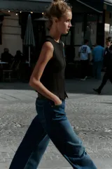 Top negro de punto, sin mangas, con cuello redondo. Presenta costuras marcadas en el frente y un bajo con abertura frontal que simula un peplum ajustado.