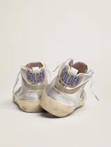 Zapatillas deportivas Golden Goose modelo Mid Star, de caña media, color plateado con detalles en dorado y beige. Presentan una estrella de gamuza en el lateral, perforaciones decorativas y cordones con logo estampado. Suela con efecto desgastado.