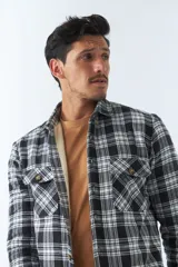 Sobrecamisa de algodón para hombre con interior de corderito, estampado a cuadros en tonos negro, blanco y azul. Tiene cierre de botones, bolsillos tipo cartera y logo en goma. El modelo usa talle M.
