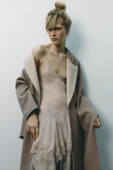 Abrigo largo color beige confeccionado en lana. Presenta cuello solapa con bufanda desmontable, manga larga, bolsillos laterales y cierre frontal cruzado con botones.