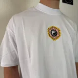 Remera blanca de corte oversize con cuello redondo y estampado pequeño en el centro del pecho con el símbolo del yin yang rodeado de llamas amarillas y naranjas.