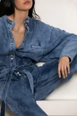 Mameluco de jean celeste con efecto nevado vintage, corte holgado, cuello mao, cierre frontal con botones y cinturón de lazo.