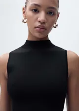 Vestido negro de punto ajustado al cuerpo, sin mangas y con cuello alto. Largo hasta la rodilla y ruedo con flecos.