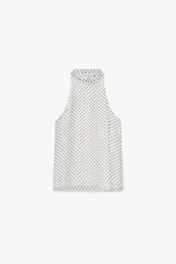 Top blanco con estampado de lunares negros, cuello halter con pañuelo y cierre con botón en la espalda.