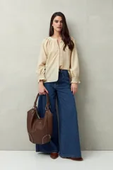 Camisa color crema de lino con cuello redondo, canesú fruncido, mangas largas amplias con puños elastizados con volado y cierre frontal con botones.