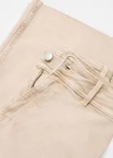 Pantalón culotte color beige de tejido tejano vaquero elástico, con tiro alto, trabillas, bolsillos delanteros y traseros, cierre de cremallera y botón, y bajo deshilachado.