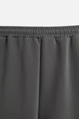 Pantalón jogger wide fit color gris oscuro, confeccionado en tejido de algodón compacto con elasticidad. Cuenta con cintura elástica ajustable con cordón, pliegues frontales, bolsillos delanteros y bolsillo trasero de parche.