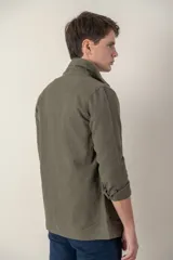 Sobre camisa color beige confeccionada en lino, de corte recto, con cuello clásico, manga larga con puños abotonados, cierre frontal con botones a tono, bolsillo de parche en el pecho y ruedo recto.