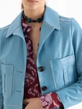 Chaqueta corta de cuero ovino color celeste claro, con cuello solapa, botones forrados y bolsillos aplicados en el frente. Las mangas presentan recortes y forma curvada.