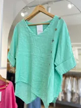 Blusa color verde agua de lino italiano, con escote en V, mangas cortas con dobladillo y cierre lateral con botones de madera.
