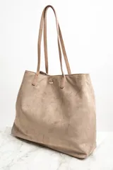 Bolso tipo tote bag grande color marrón, confeccionado en cuero vegano, con doble asa de hombro y detalle de pañuelo estampado atado a una de las asas.