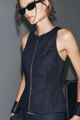 Top de denim color blanco, de cuello redondo y sin mangas. Cierre frontal con cremallera metálica.