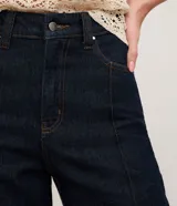 Pantalón de jeans de tiro alto, corte recto y color azul oscuro. Presenta costuras verticales contrastantes visibles en el frente de ambas piernas.