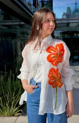 Camisa blanca traslúcida con botones y estampado de flores anaranjadas.