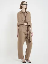 Chaleco marrón de gabardina con corte recto y estilo utilitario. Tiene cierre frontal con tirador de flecos largos en cuero y bolsillos grandes con tapa en el frente.