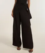 Pantalón pantalona de sastrería color negro, confeccionado en tejido texturizado. Presenta corte amplio, superposición lateral con lazo y tiro alto.