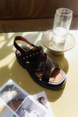 Sandalias de cuero marrón con tiras cruzadas y detalles de tachas. Suela de goma negra con plataforma.