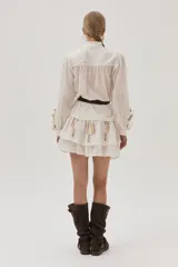 Blusa blanca de viscosa con cuello mao, cierre frontal con botones, mangas largas abullonadas con volados y bordados florales.