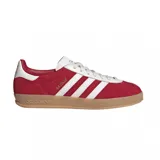 Zapatilla Adidas modelo Gazelle Indoor, con capellada de gamuza color rojo, tres franjas laterales y refuerzo de talón en cuero blanco. Posee cordones blancos y suela de goma color caramelo.