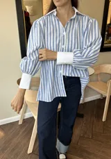 Camisa celeste y blanca a rayas verticales, de corte amplio y mangas largas con puños anchos.