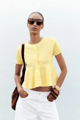 Chaqueta color amarillo claro de tejido de punto, con cuello redondo, manga corta, cierre frontal con botones y bajo evasé.