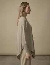 Poncho de tejido lurex color verde oliva con brillo sutil, de corte amplio y manga larga con puños acanalados. Presenta un bajo asimétrico con caída diagonal.