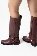 Botas de cuero color bordó con textura croco, caña alta con correa decorativa con argolla metálica y taco bajo.