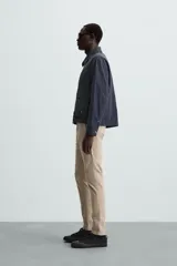 Pantalón chino color beige, corte skinny fit, confeccionado en tejido con mezcla de algodón y elasticidad. Cuenta con bolsillos frontales y traseros. Cierre frontal con cremallera y botón.