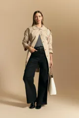 Trench color beige de corte clásico con cuello amplio, botones frontales, detalles en los hombros y mangas largas.