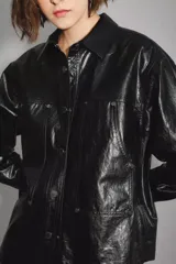 Campera negra de cuero sintético con acabado brillante, cuello camisero, cierre frontal con botones y dos bolsillos delanteros con solapa.