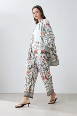 Pantalón de corte recto con estampado floral en tonos naranja, rojo, verde y marrón sobre fondo blanco. Presenta cintura elástica y ruedo con diseño geométrico.