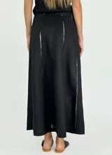 Pollera larga negra de corte amplio, con costuras verticales que simulan pliegues y terminaciones deshilachadas. Se combina con una musculosa negra de escote redondeado.