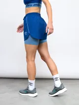 Short deportivo negro de entrenamiento para mujer, con calza interna integrada. El short exterior es de poliéster y presenta un ribete blanco en los laterales.