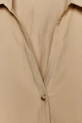 Camisa color beige de cuello solapa con escote pico y manga corta ancha acabada en vuelta con trabilla y botón. Cierre frontal con botones.