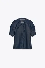 Camisa de denim azul oscuro con cuello redondo ajustable con lazadas, mangas cortas abullonadas, efecto lavado, bajo recto y cierre frontal con botones.