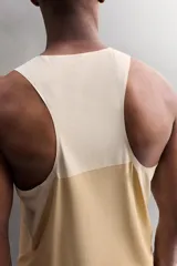 Camiseta deportiva sin mangas color beige, confeccionada en tejido técnico ligero y elástico con estructura perforada. Tiene cuello redondo amplio, sisas con acabados termofijados, bajo con aberturas laterales y logo estampado.