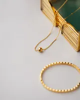 Collar asimétrico dorado con cadena de bolitas y dije esférico.