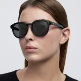 Lentes de sol negros con montura redonda de diseño angular y detalles geométricos. Lentes polarizadas alemanas con protección UV400, recubrimiento anti-scratch y superhidrofóbico. Fabricados con material bio-based G850 y patillas de propionato de celulosa.