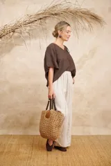 Blusa de lino color beige, con detalles de punto escama en escote y mangas, y prendedor de flor en el hombro. Talle único.