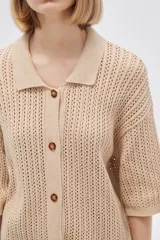 Remera de punto calado color beige, con cuello polo, mangas cortas y cierre frontal con botones.